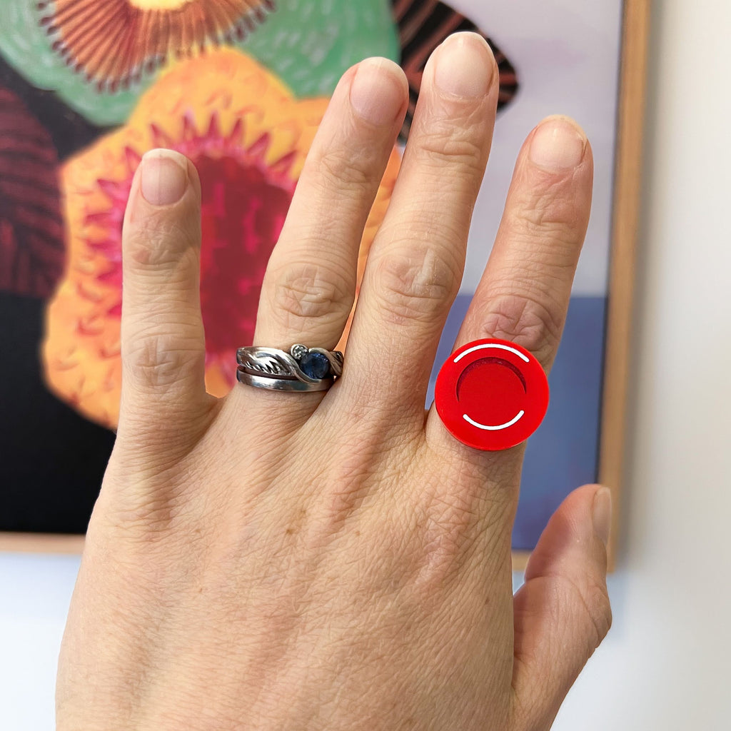 A hand modelling a Red Blood Cell Earring, handmade and hand painted from red laser cut acrylic.