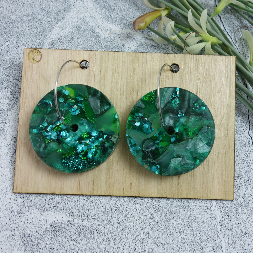 Recycled acrylic earrings in mixed green tones. Earrings comprise of acrylic discs with hole in the center, hanging from stainless steel hoops. 
