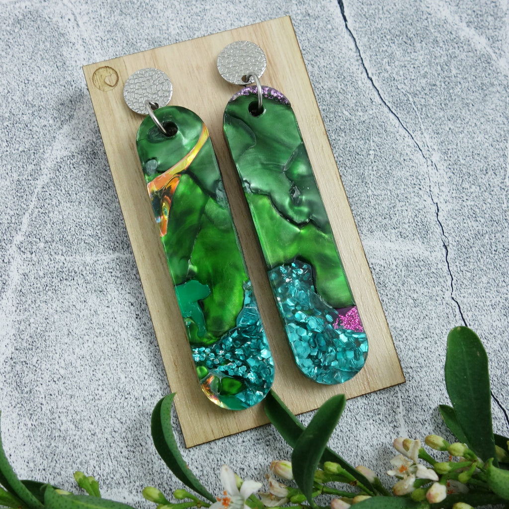 Long drop earrings made from recycled acrylic in green tones. The earrings hang from textured stainless steel earring toppers.