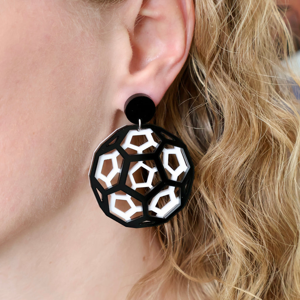 Black and white bucky ball earrings in laser cut acrylic, being modelled.