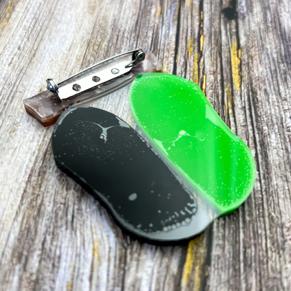 The back view of a monarch chrysalis laser cut acrylic brooch, showing the stainless steel brooch pin and rolling clasp. 