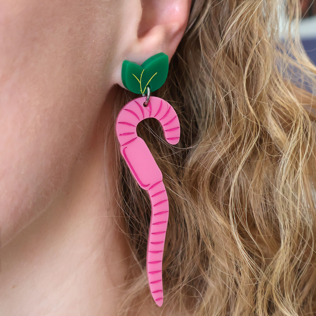 Pink Acrylic Earth Worm Earrings hanging from Green Leaf Toppers, being modelled.