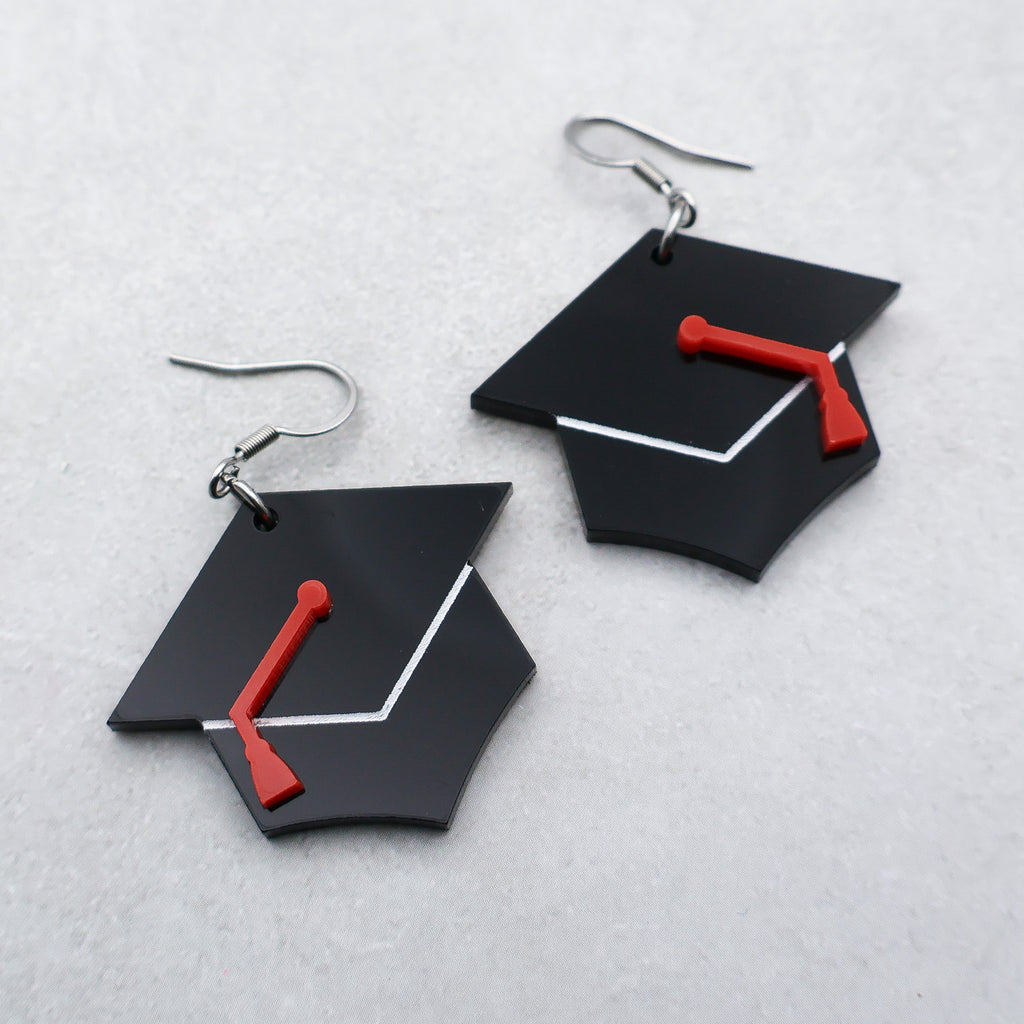 Black acrylic graduation cap earrings with red acrylic tassles and fishhook toppers.