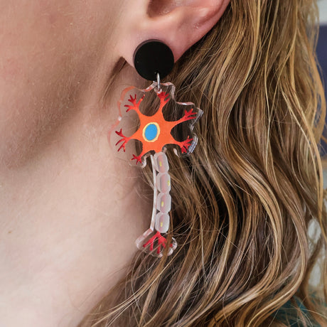 Laser cut acrylic neuron earrings being modelled. Earrings are cut from transparent acrylic, with the neuron design engraved and handpainted. The neurons hang from black earring toppers.