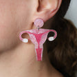 Statement sized Pink Acrylic Uterus dangle earrings being modelled on an ear.