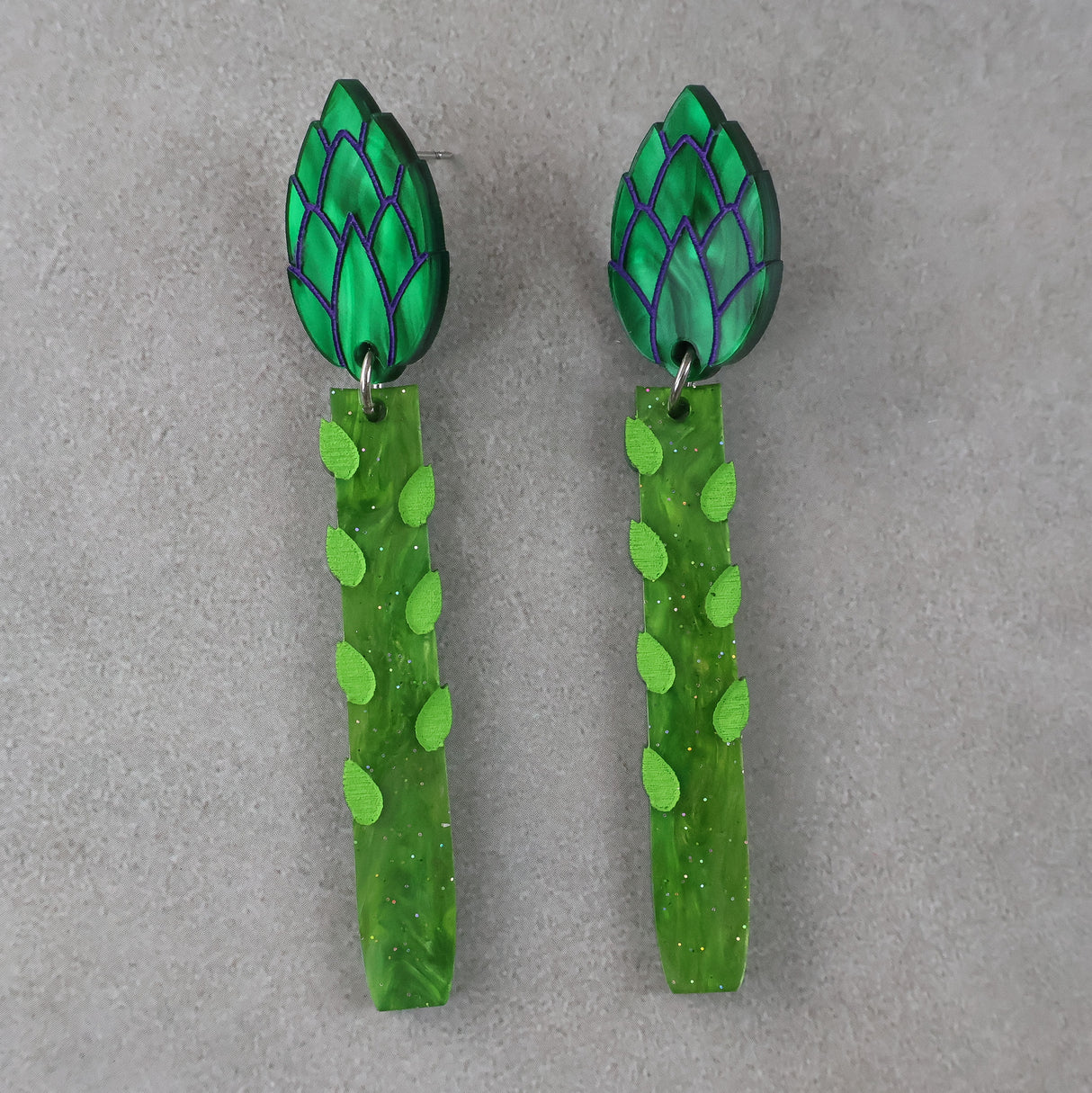 Green asparagus acrylic earrings with leaf-shaped toppers earrings on a grey background