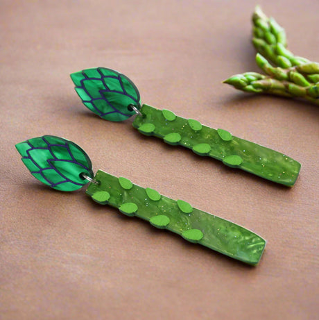 Angled view of green asparagus acrylic earrings with leaf-shaped toppers earrings on a grey background