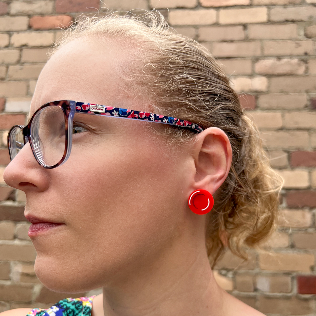 A red blood cell stud being modelled by the maker, a blonde woman with glasses. Studs are laser cut and handpainted from acrylic. 