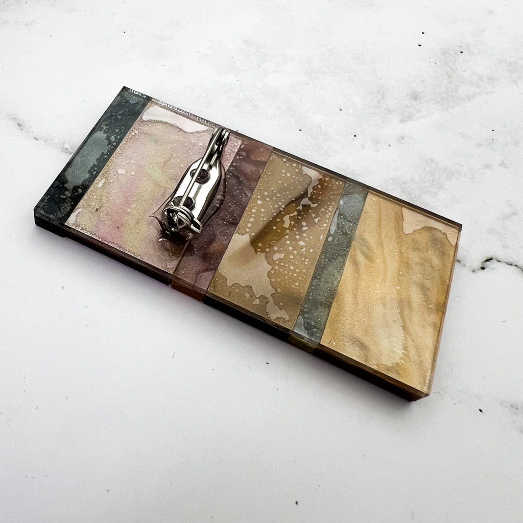 A back view of a sedimentary layers acrylic brooch, showing the stainless steel brooch pin with rolling clasp. 