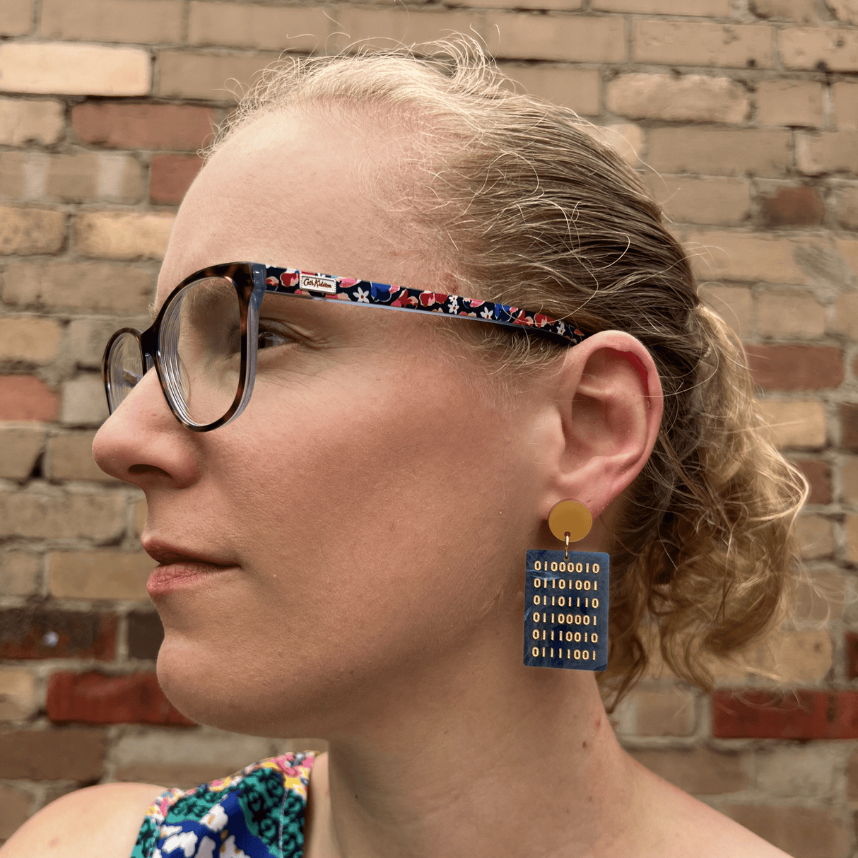 A pair of binary acrylic earrings being modelled by a blonde woman with glasses