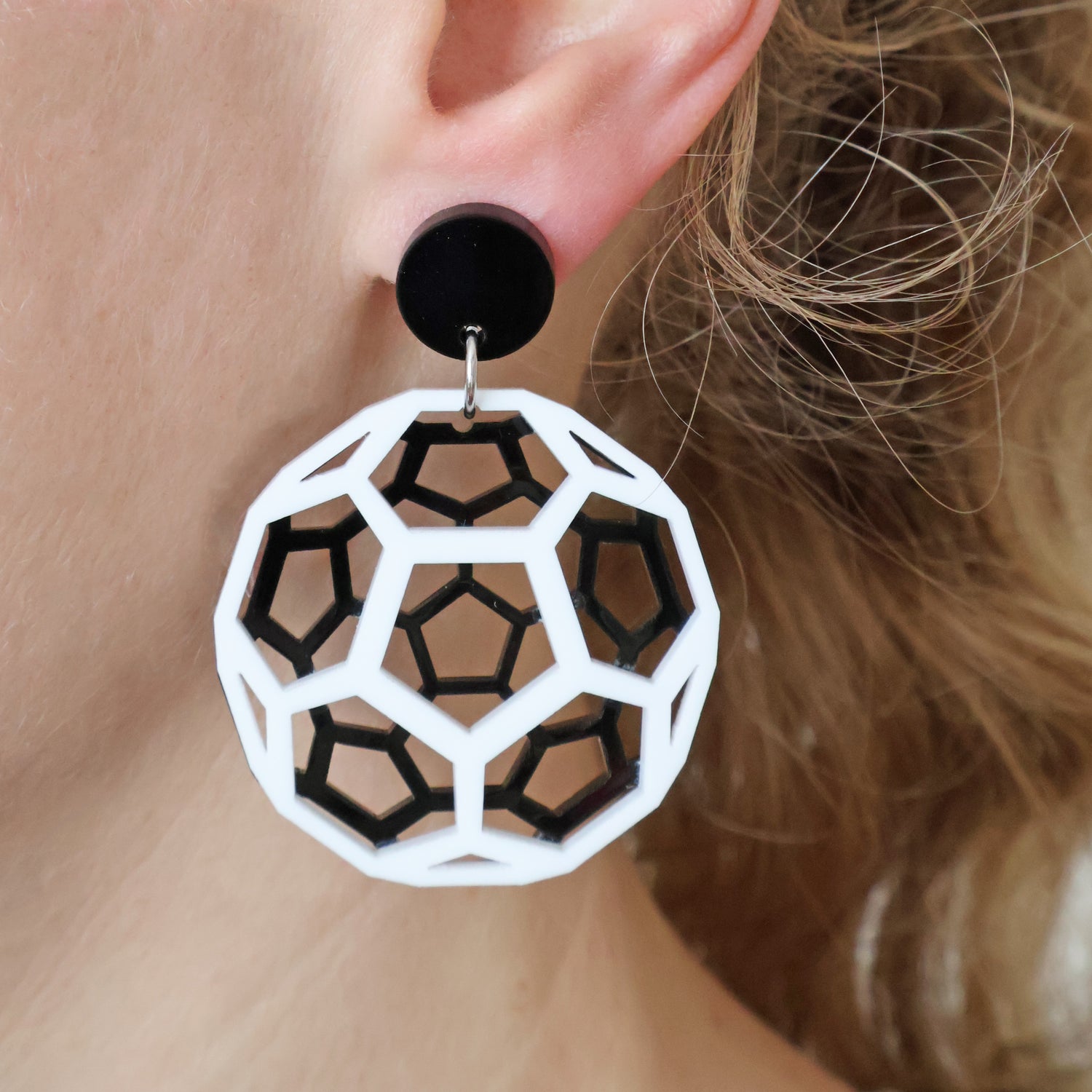 Geometric black and white acrylic earrings worn depicting a bucky ball worn by a person with blonde hair.