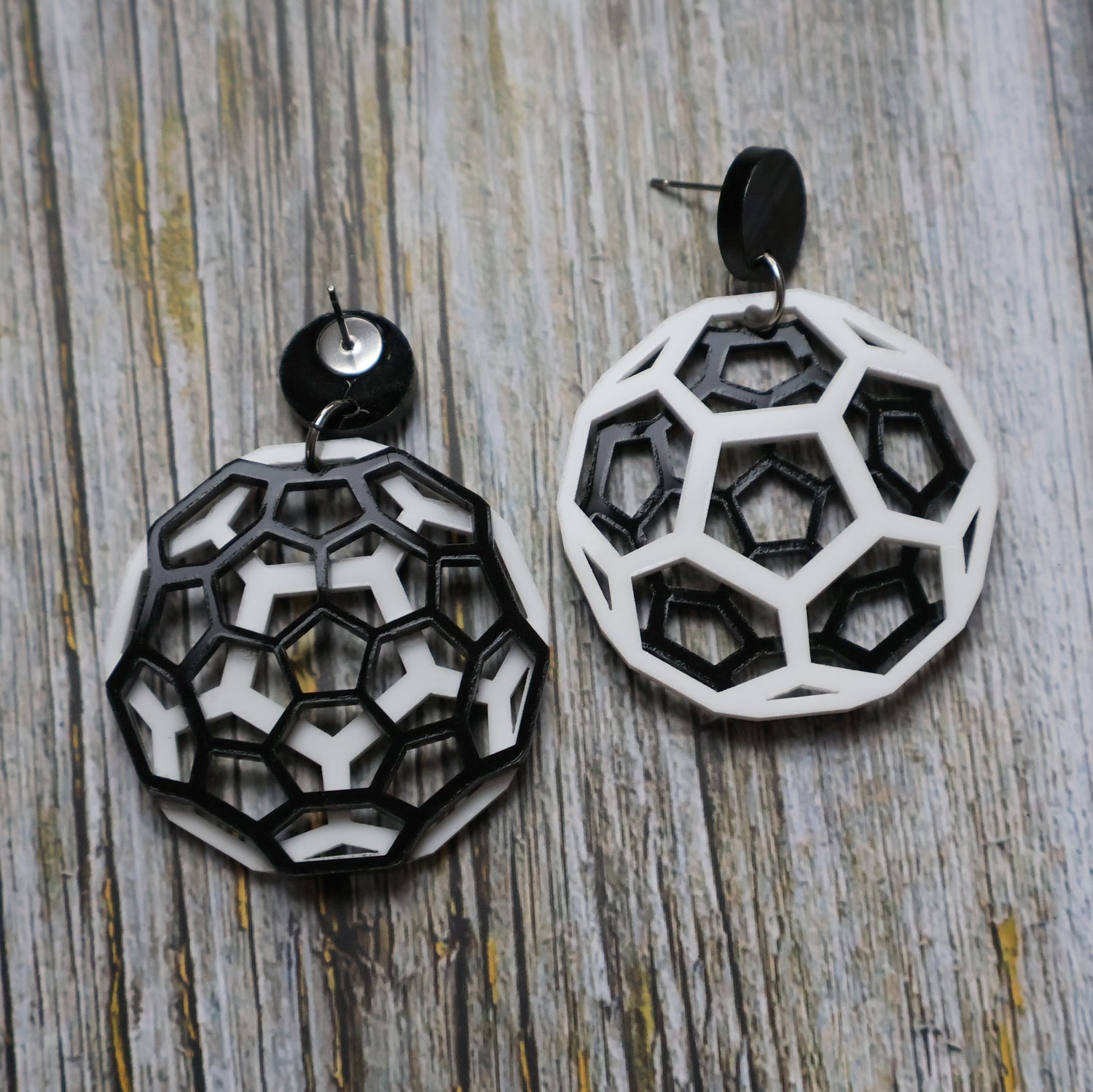 Geometric black and white earrings shaped like carbon bucky balls on a wooden surface. One earring is turned to show the back.