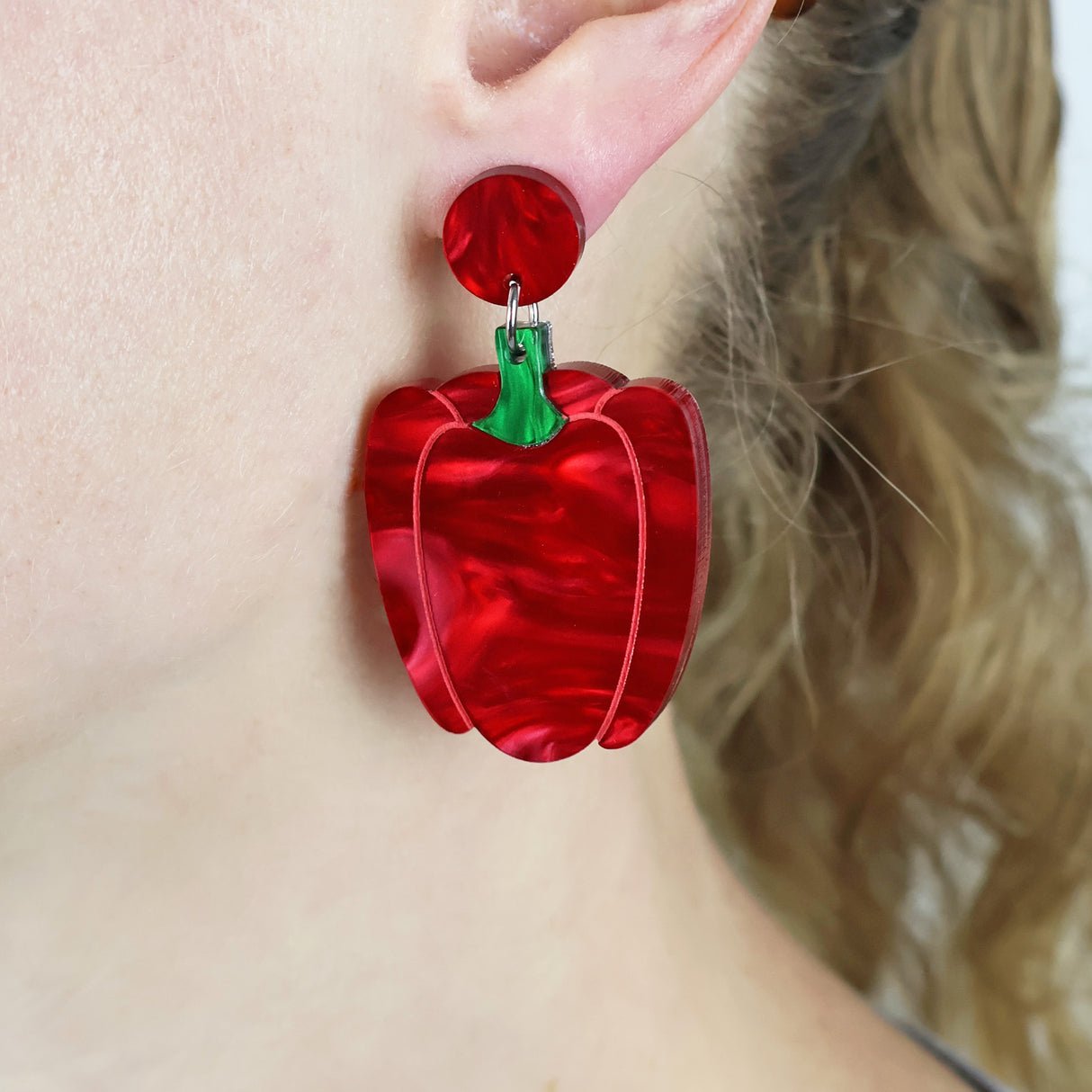 Red capsicum shaped earrings worn by a person with blonde hair.