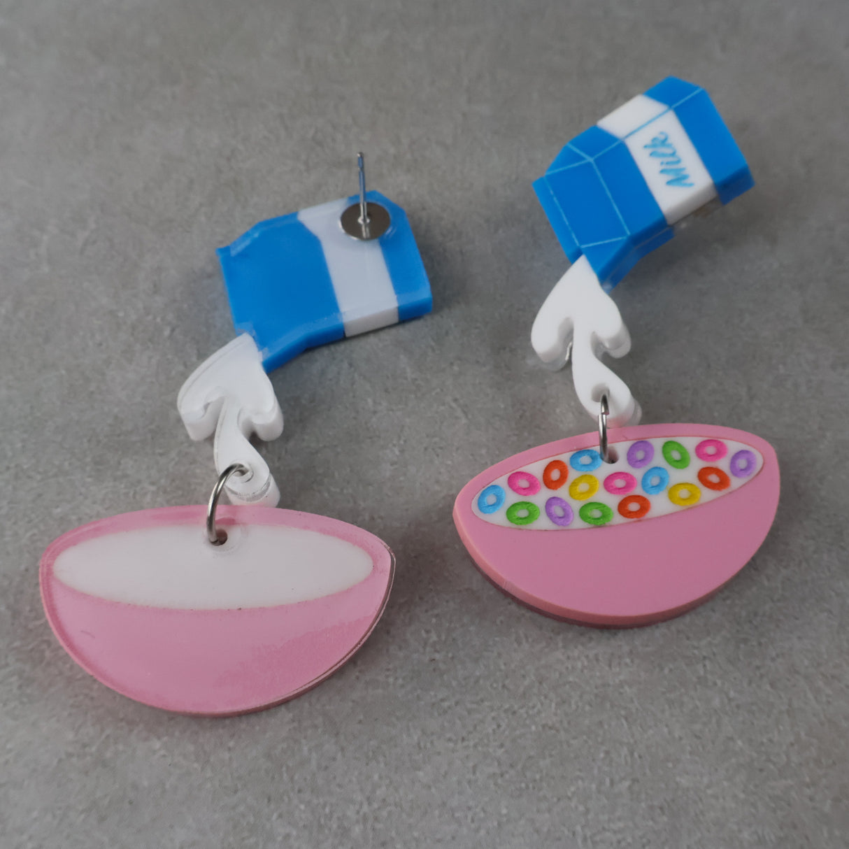 A pair of acrylic earrings shaped like a milk carton pouring into a bowl of cereal. The back view of one earring sows the stainless steel post.