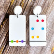 A pair of Chromatography earrings featuring white rectangular shapes with a series of colorful dots arranged in a specific pattern, hanging from white toppers.