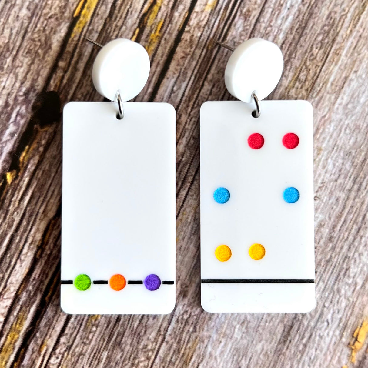 A pair of Chromatography earrings featuring white rectangular shapes with a series of colorful dots arranged in a specific pattern, hanging from white toppers.