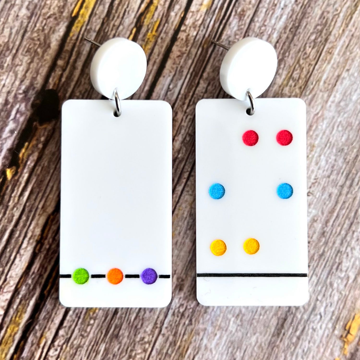A pair of Chromatography earrings featuring white rectangular shapes with a series of colorful dots arranged in a specific pattern, hanging from white toppers.