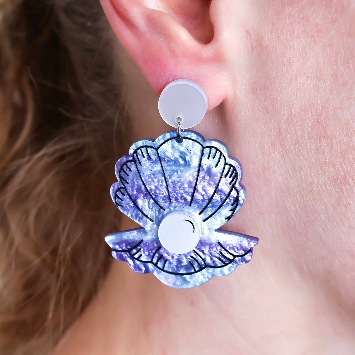 Clam Shell-shaped acrylic earrings with a glittery purple design worn by a person. Marine Biology Science Jewellery