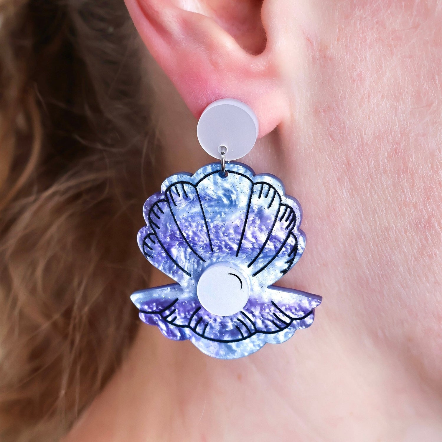 Clam Shell-shaped acrylic earrings with a glittery purple design worn by a person. Marine Biology Science Jewellery