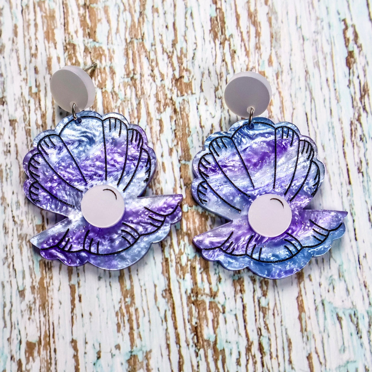 Pair of purple and blue clam earrings on a wooden surface