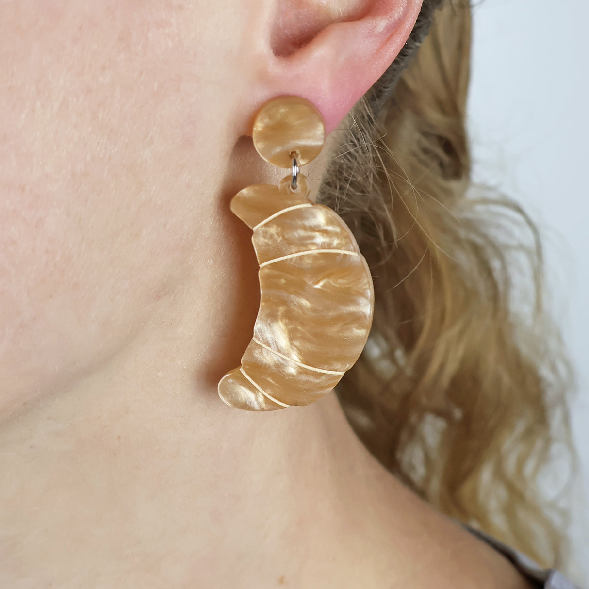 Caramel toned acrylic croissant earrings worn by a person. Earrings have matching round acrylic toppers.