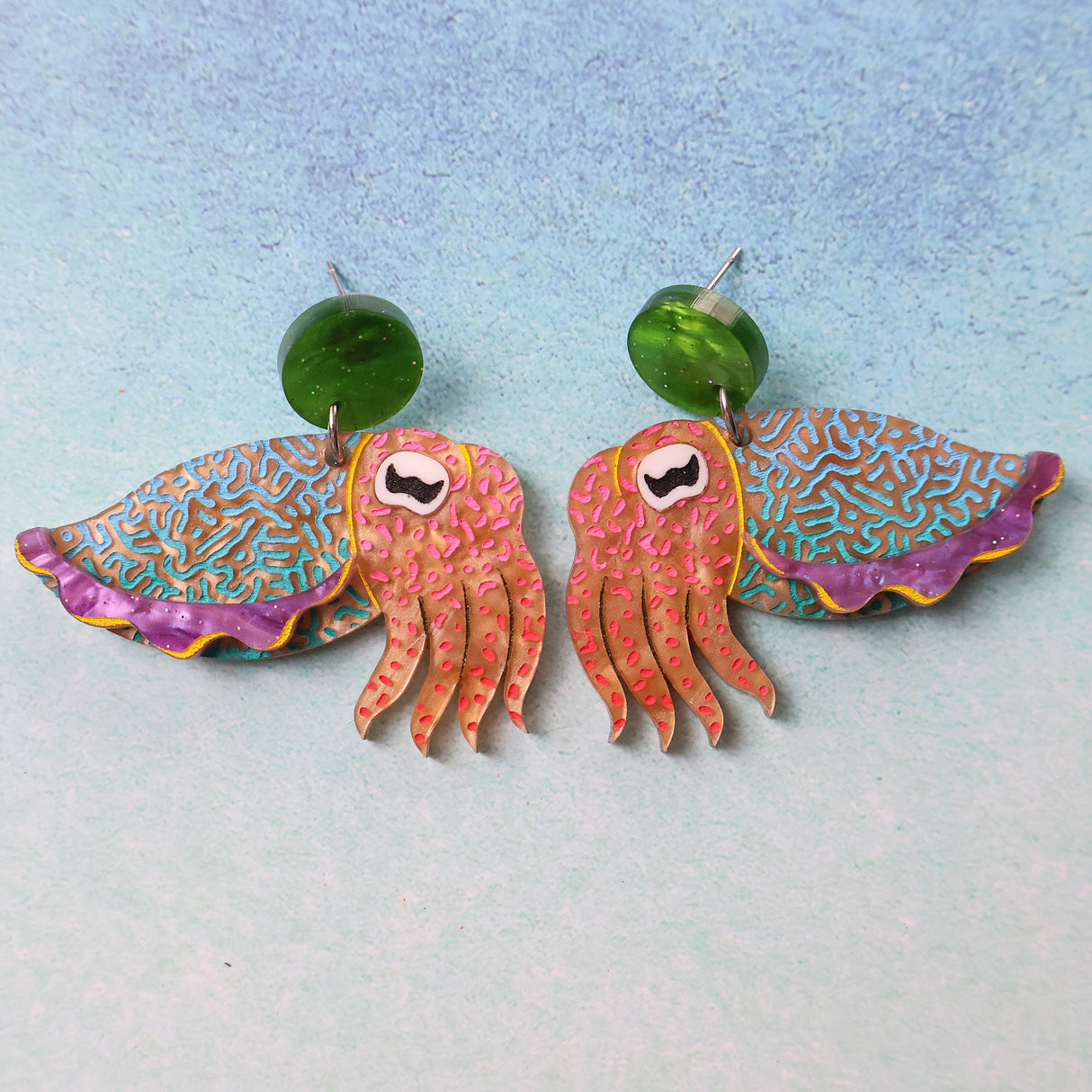 Colourful cuttlefish shaped earrings on a light blue background