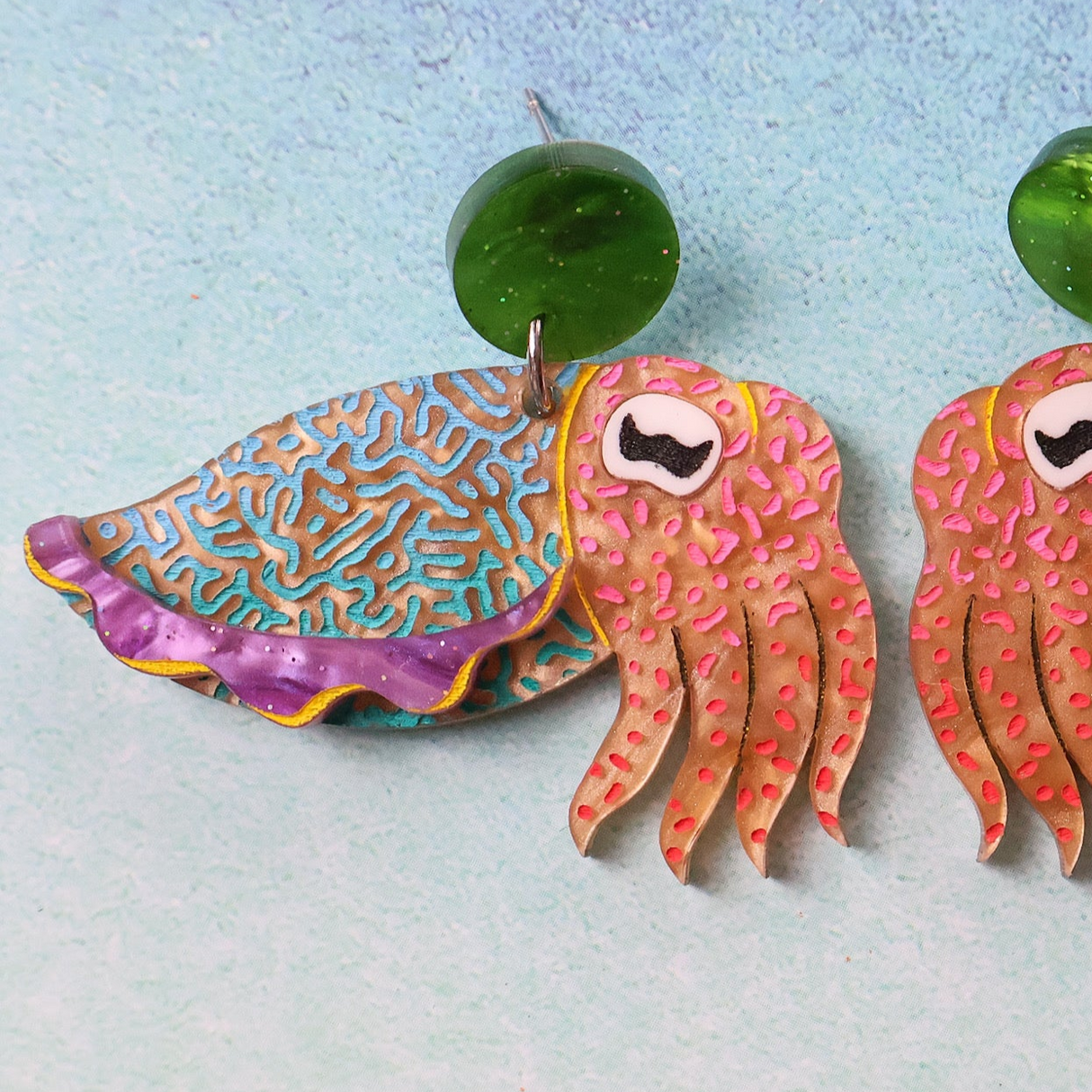Colorful cuttlefish-shaped earrings on a light blue background