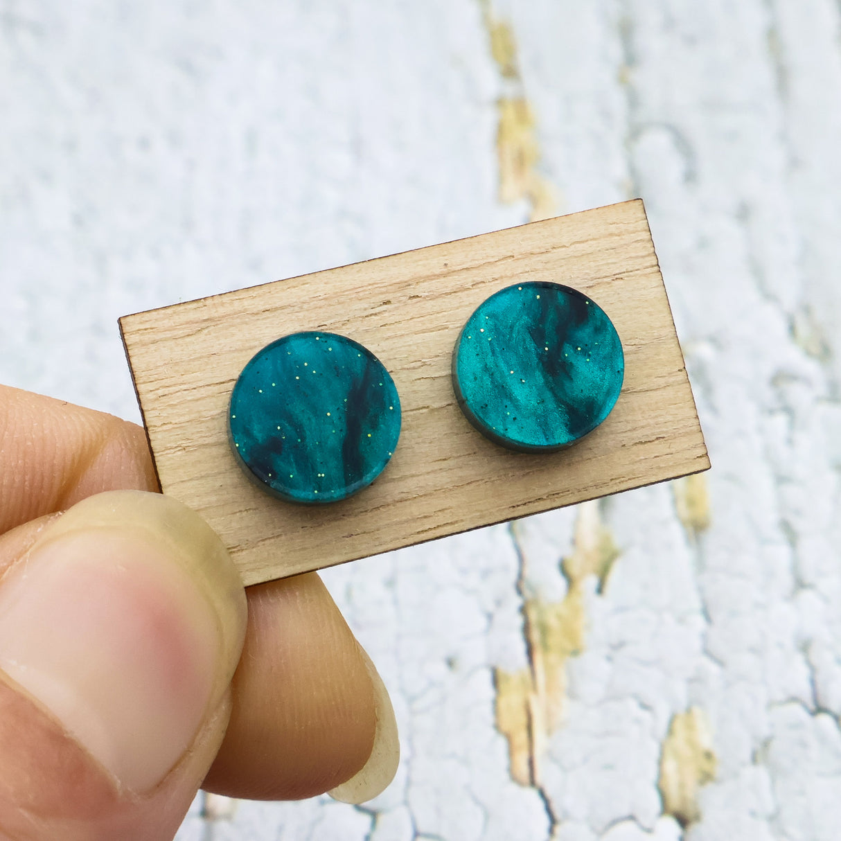 A pair of small swirly 10mm diameter green acrylic studs on a wooden backing card.