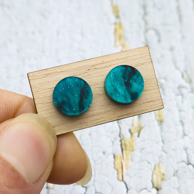 A pair of small swirly 10mm diameter green acrylic studs on a wooden backing card.