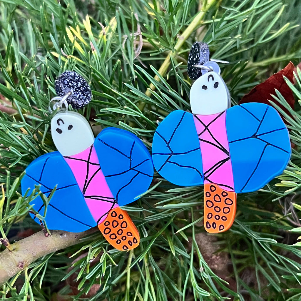 Acrylic dragonfly earrings lying in the grass, in the style of a small child's drawing. Laser cut from acrylic.