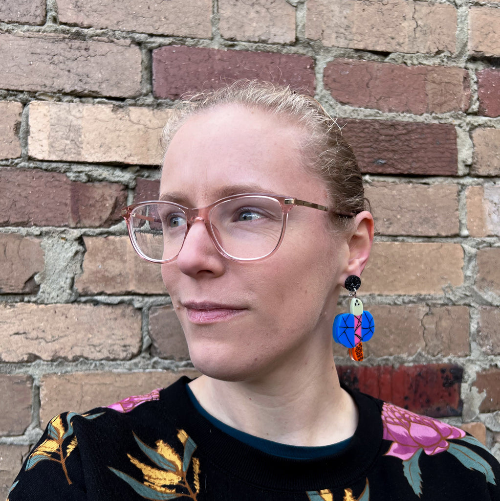 Acrylic dragonfly earrings being modelled by the maker, a blonde woman with glasses.