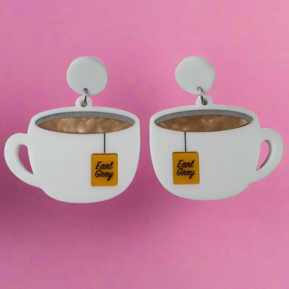 Front view of white tea cup acrylic earrings with Earl Grey tea bag tags and round white toppers against a grey background