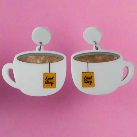 Front view of white tea cup acrylic earrings with Earl Grey tea bag tags and round white toppers against a grey background