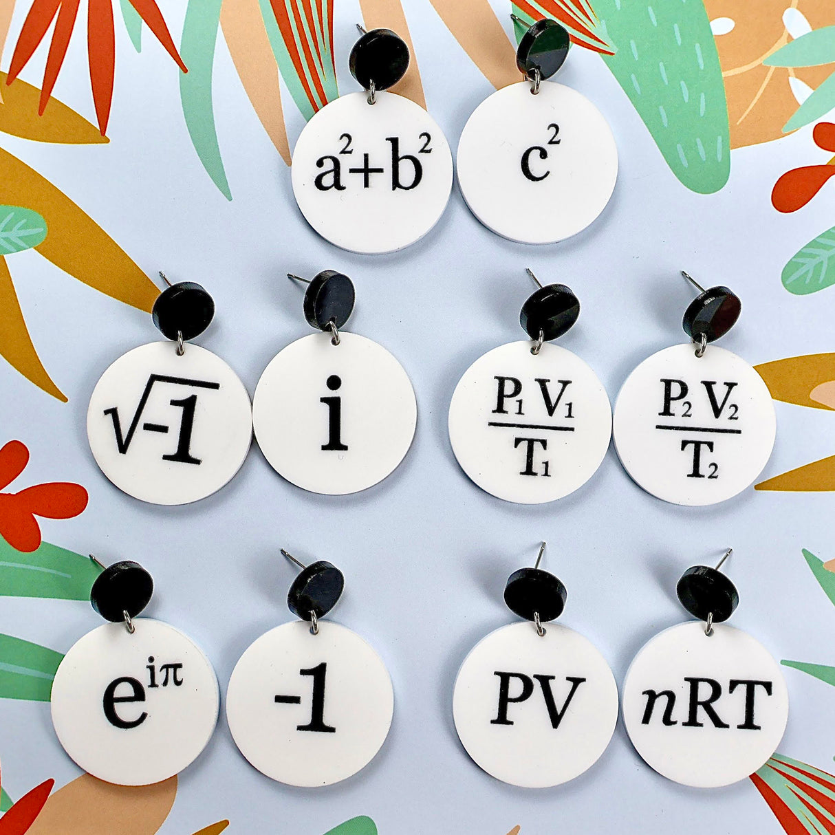 A collection of white dangle acrylic  earrings, each with a different mathematical equation printed in black.