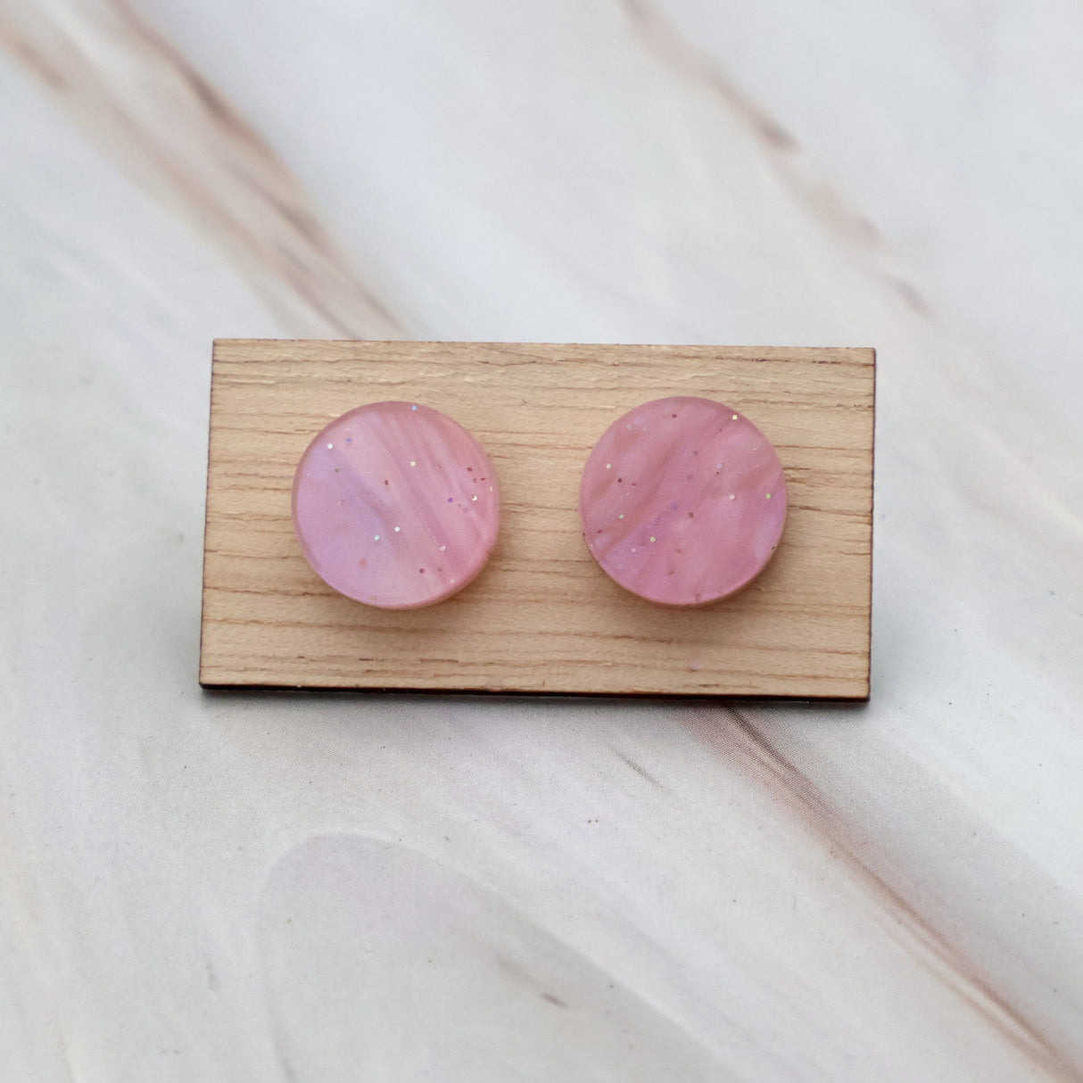 A pair of pink acrylic 10mm diameter stud earrings on a wooden display card.