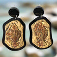 A pair of earrings with a brown fish skeleton cabochon design mounted in a black acrylic border, with black acrylic toppers.