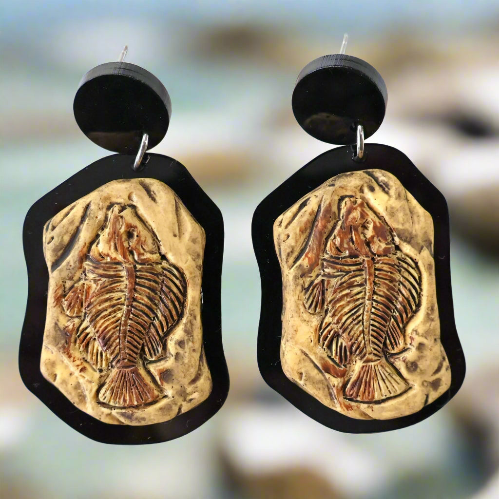 A pair of earrings with a brown fish skeleton cabochon design mounted in a black acrylic border, with black acrylic toppers.