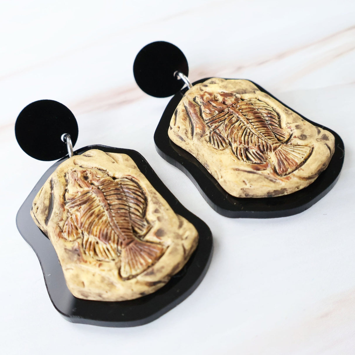 Fish fossil-themed earrings on a white background.