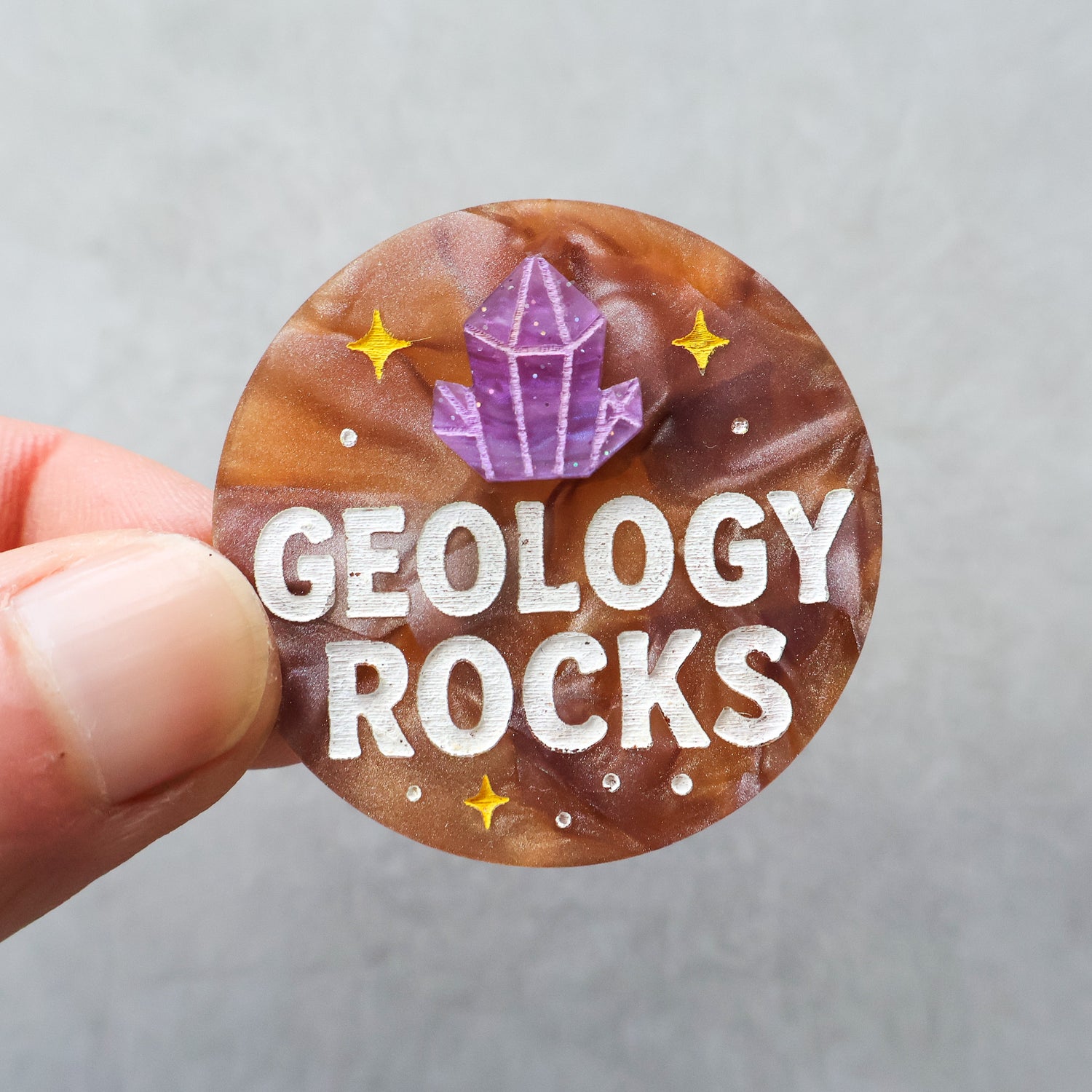 Round badge or brooch with 'Geology Rocks' text and crystal illustration held by a hand