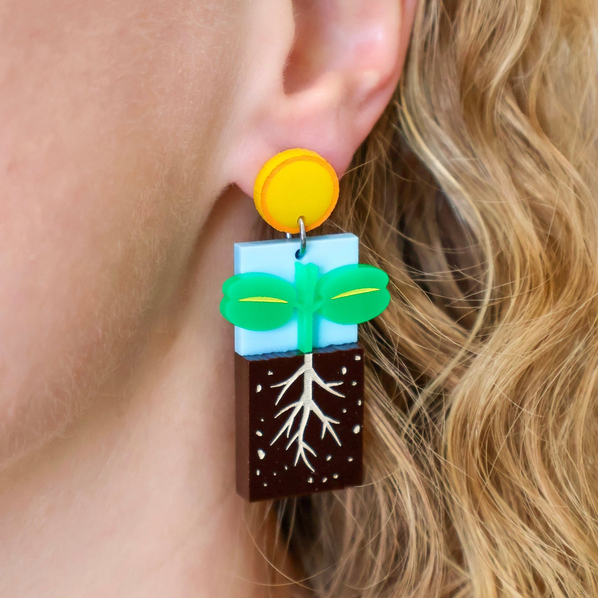 A germination earring being modelled, showing a seedling growing under a yellow 'sun' earring topper. Laser cut and handpainted from acrylic.
