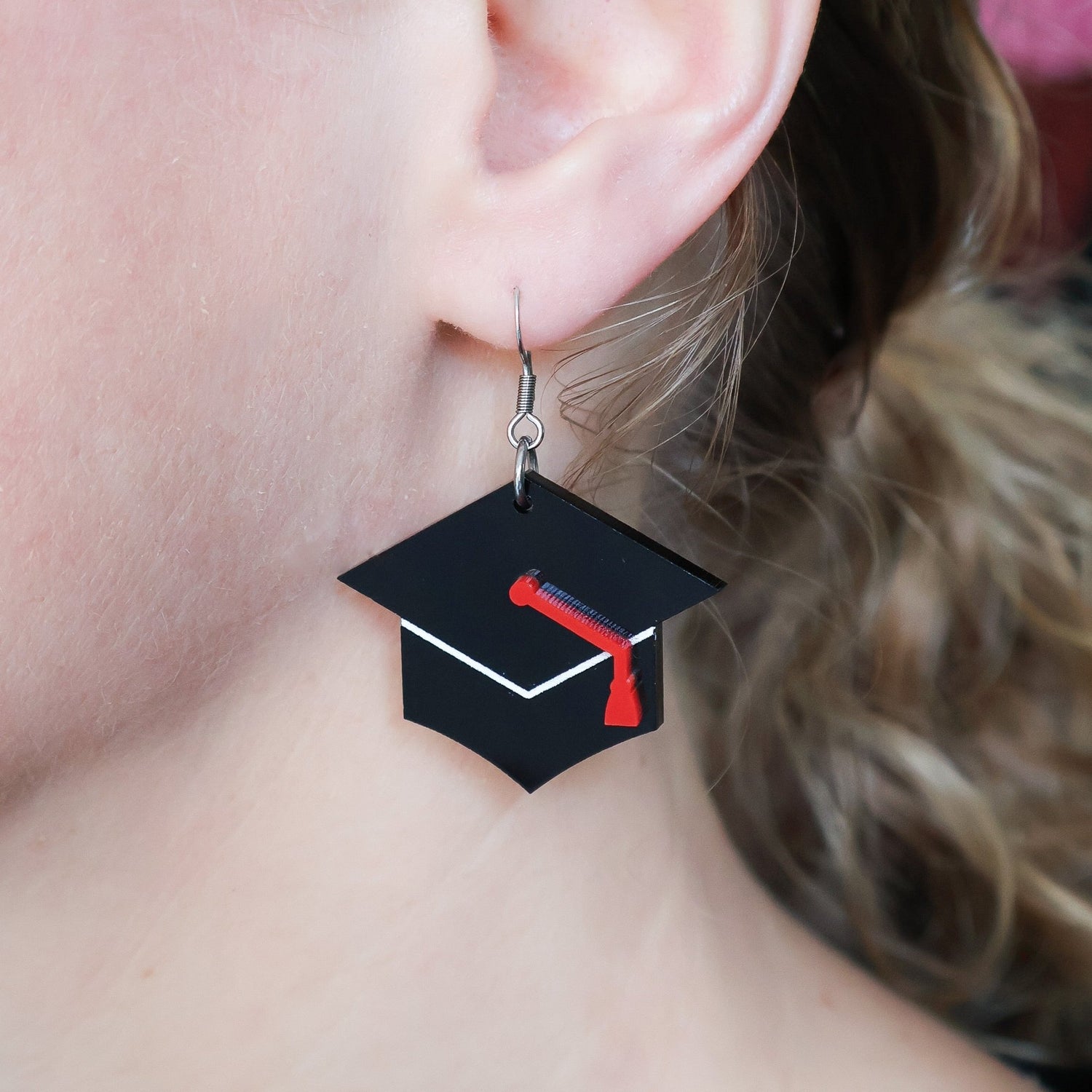 Graduation cap earrings being modelled. Black caps with red ribbon and stainless steel french hooks.