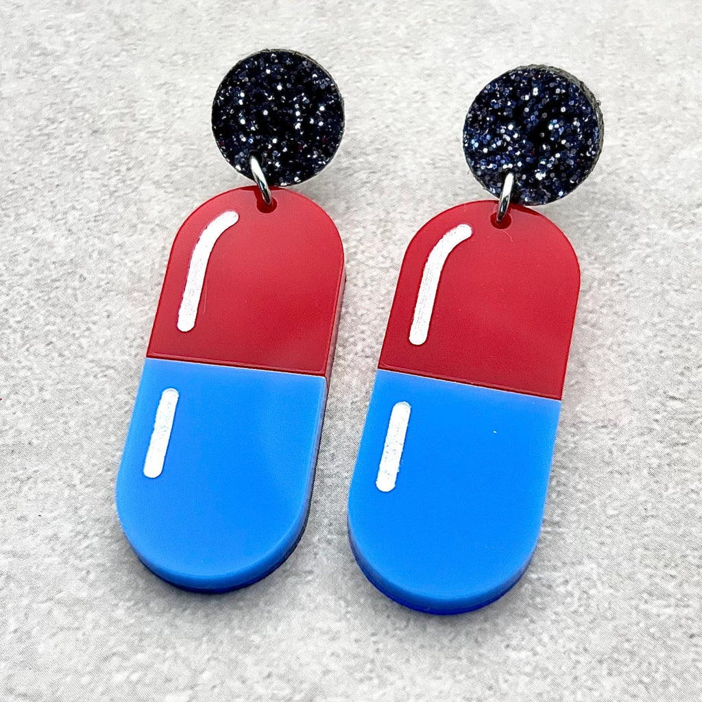 Red and blue pill earrings hanging from black glittery acrylic toppers. Laser cut from acrylic.