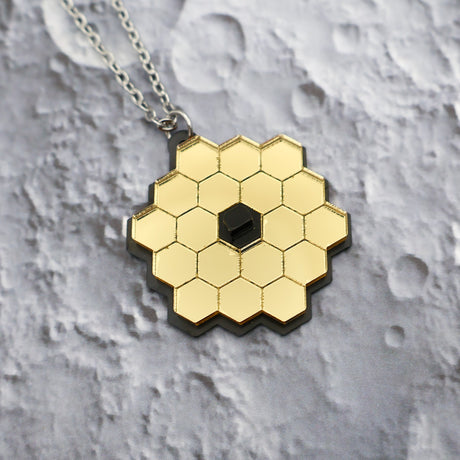 Closeup of JWST (James Webb Space telescope) pendant against a lunar backdrop, showing gold mirror acyrlic and stainless steel chain.