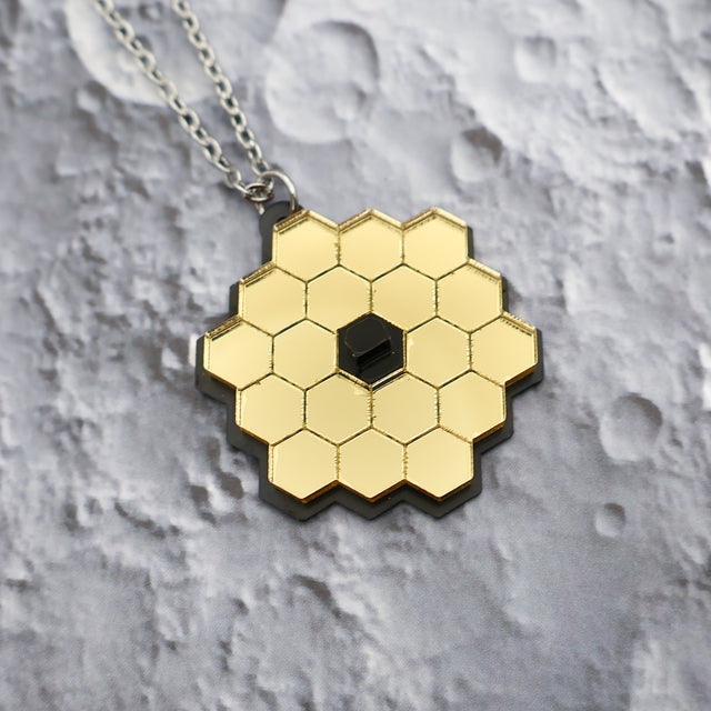 Closeup of JWST (James Webb Space telescope) pendant against a lunar backdrop, showing gold mirror acyrlic and stainless steel chain.