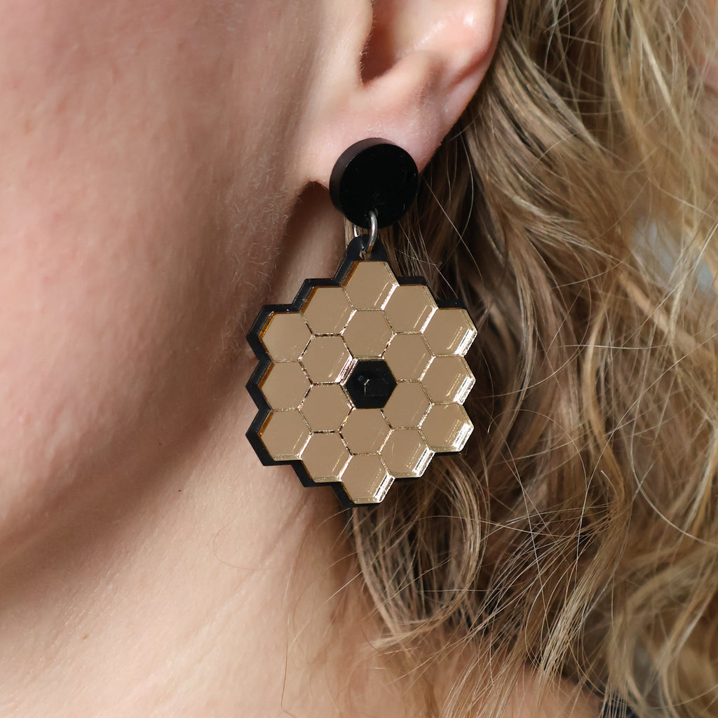 James Webb Space Telescope Earrings constructed from gold mirror acrylic and black acrylics, being modelled. 