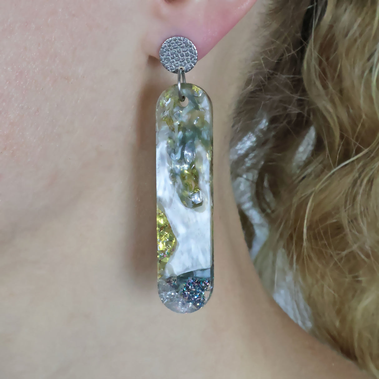 long oval shaped recycled acrylic earrings with stainless steel toppers being modelled on the ear of a person with blonde hair.
