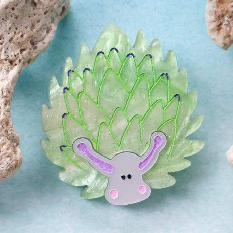 Green leaf sheep acrylic brooch against a blue background with coral props around