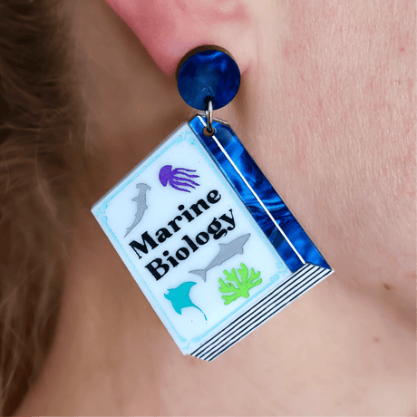 Earring with 'Marine Biology' design on a book-shaped dangle, worn on an ear.