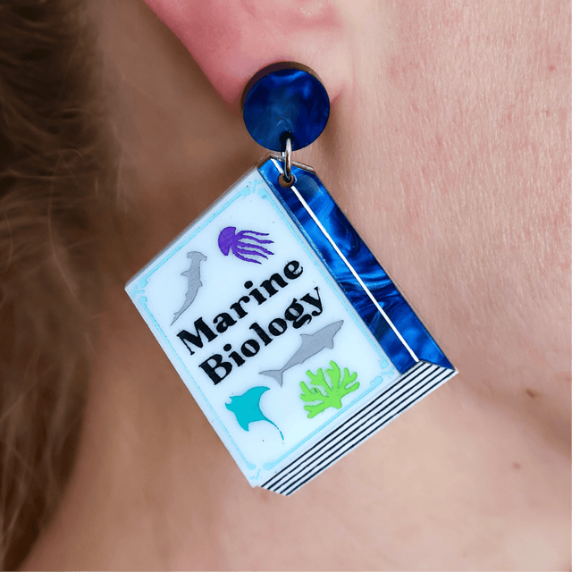 Earring with 'Marine Biology' design on a book-shaped dangle, worn on an ear.
