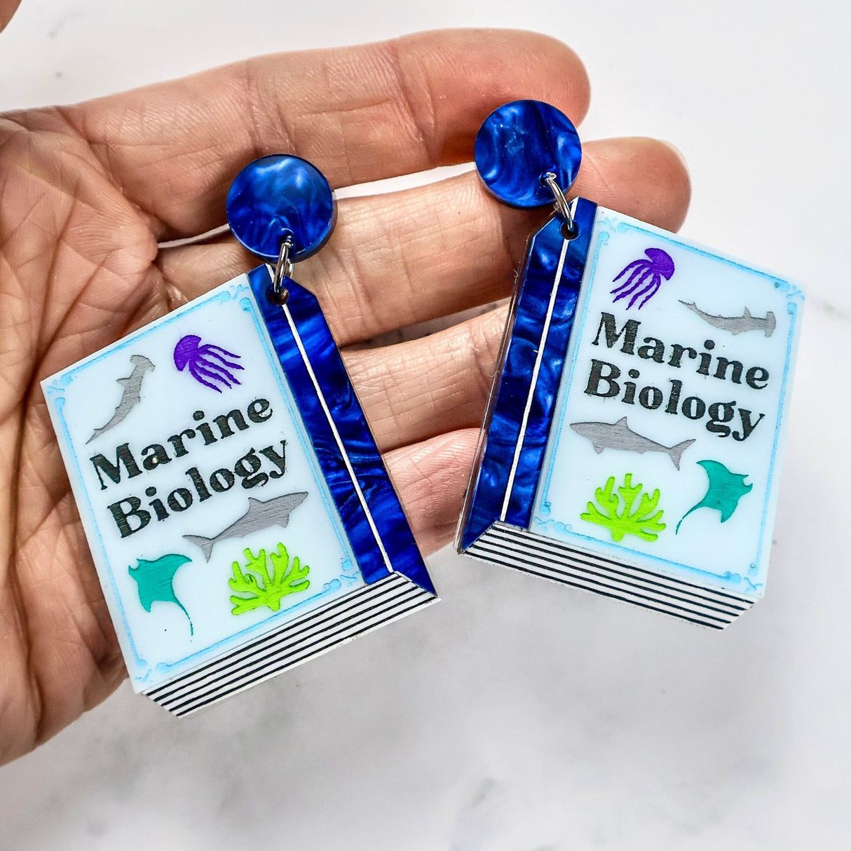 Marine Biology-themed earrings held in a hand against a white background